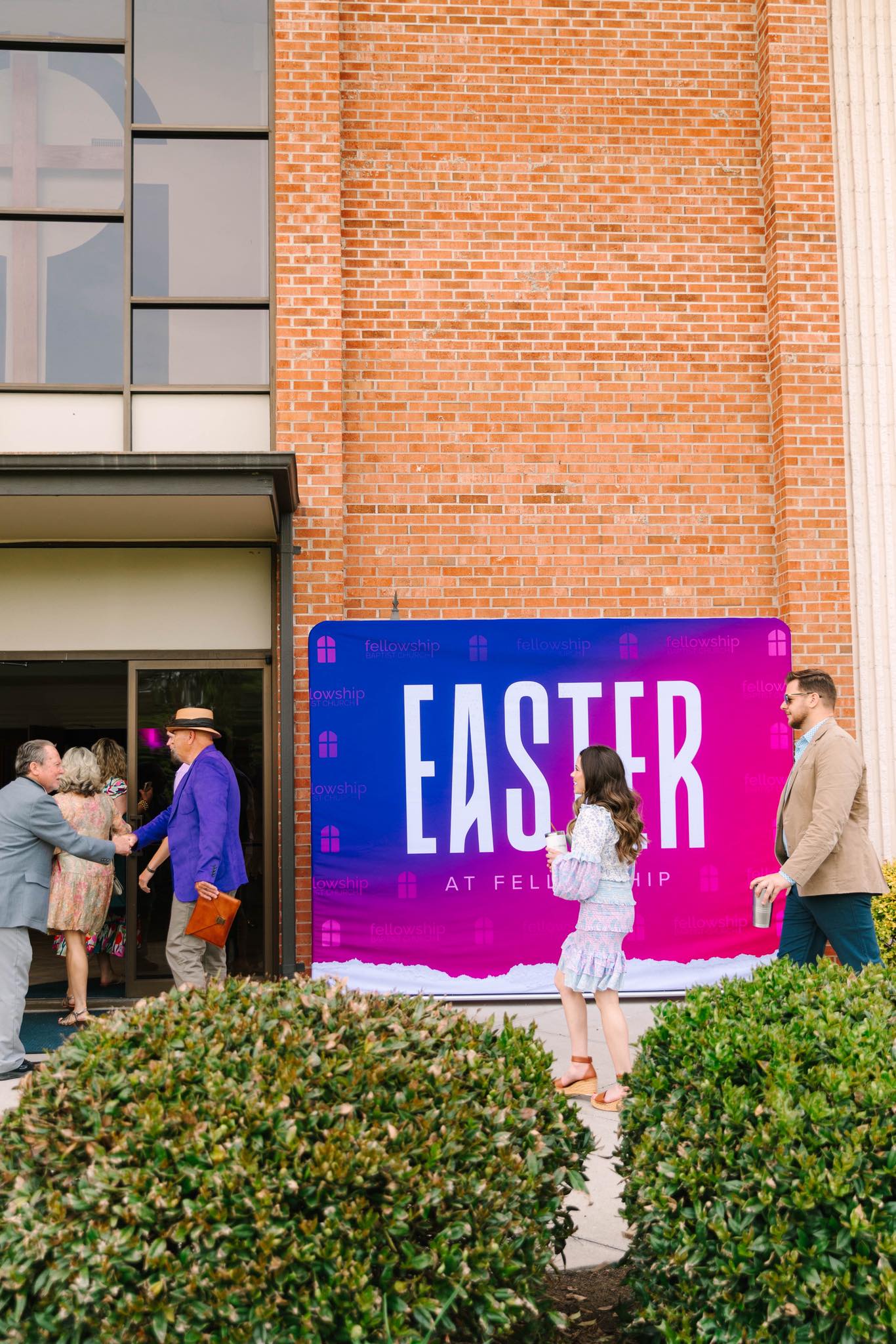 Guests arriving at Fellowship Baptist Church in Durham, NC, with a large purple and pink “Easter at Fellowship” backdrop displayed outside the entrance.