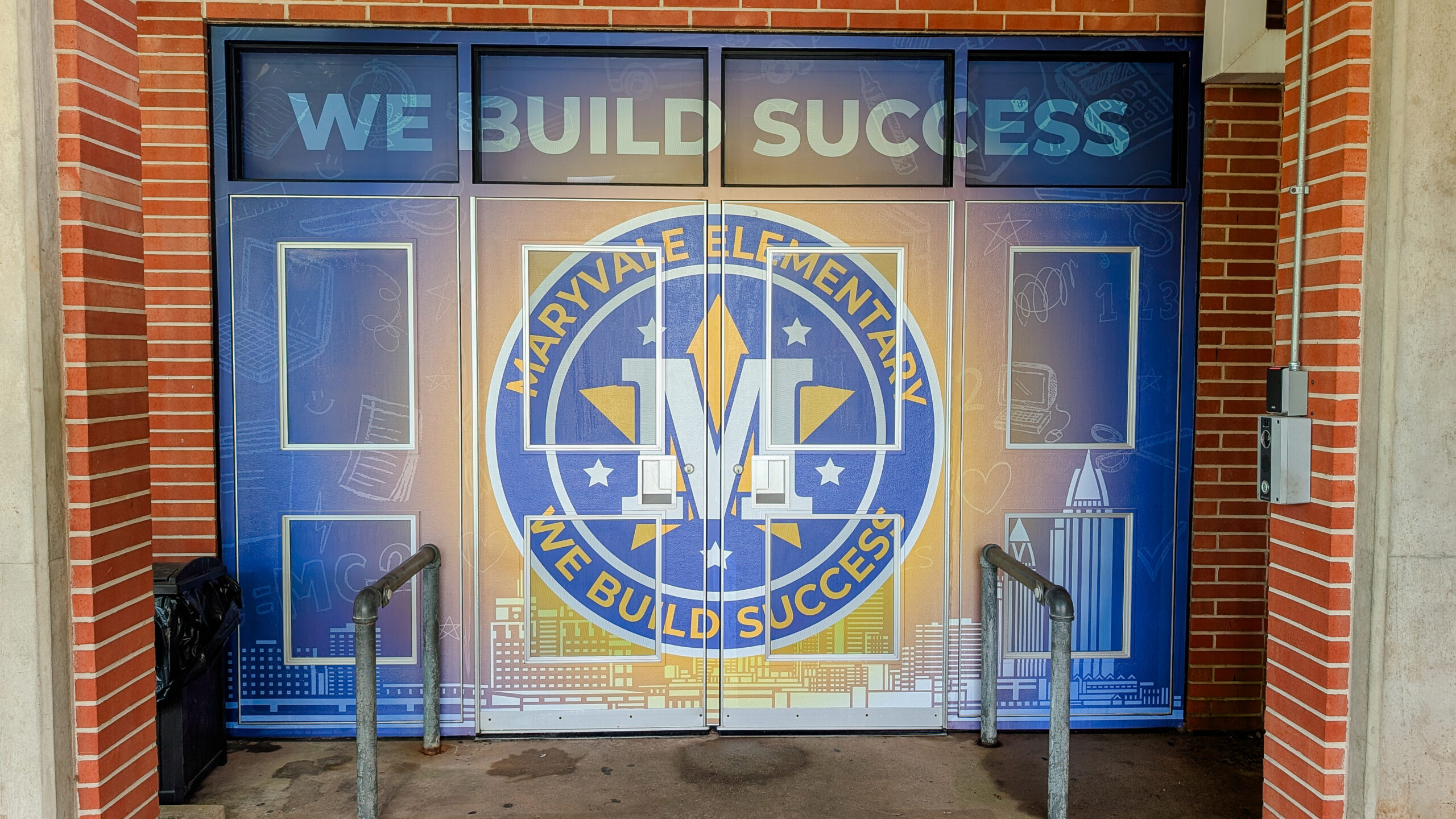Front entrance of Maryvale Elementary School featuring full window and door wraps with “We Build Success” branding and colorful pillar graphics.